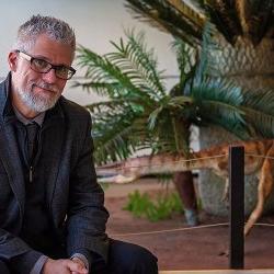 Dr. Scott Kight sitting by the dinosaur exhibit in the CELS Atrium